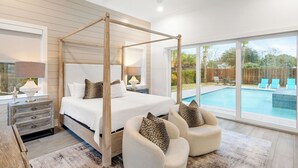 Quarto com cama de dossel, mesa de cabeceira, luminária e vista para uma piscina ao ar livre.