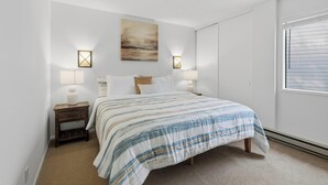 Ein Schlafzimmer mit einem Bett, Nachttischlampen, einem Wandbild und einem Fenster mit Jalousien.