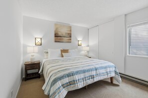A bedroom with a bed, bedside lamps, a wall-mounted artwork, and a window with blinds. - Indian Springs Retreat | Elkhorn Amenities (Sun Valley)