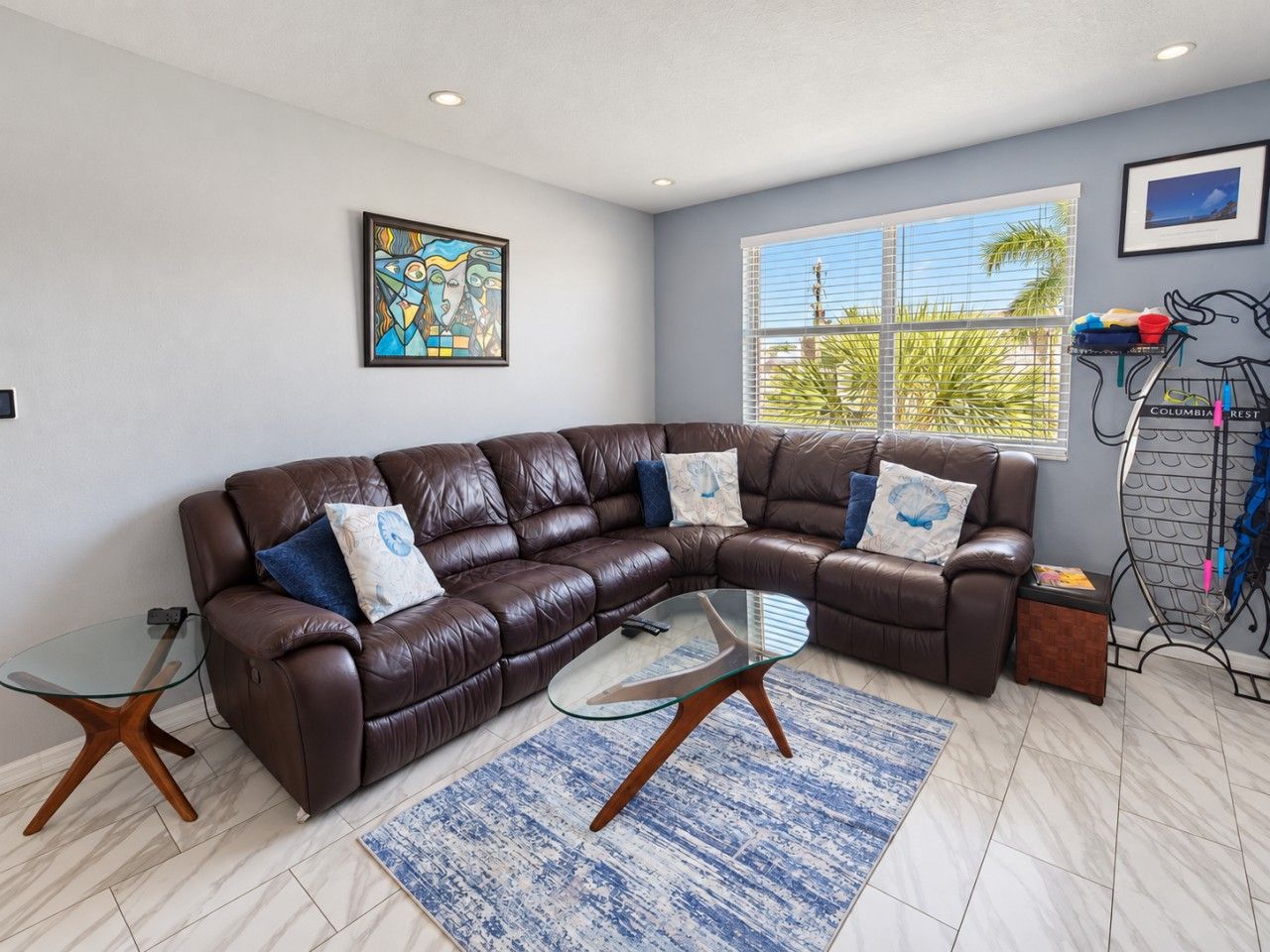 A modern living room with a brown leather sectional sofa, a glass coffee table, and a blue patterned rug.