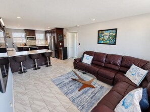 Een moderne woonkamer met een bruine leren bank, een salontafel en een keuken in de achtergrond.