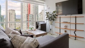 Een moderne woonkamer met een groot raam, een flatscreen televisie, een bank, een salontafel en een plant.