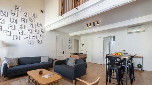 Amplia sala de estar con un conjunto de sofás, una mesa de centro de madera, una silla de mimbre, una mesa de comedor con sillas y una cocina al fondo.