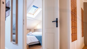 Una habitación con tragaluz, una cama con manta azul y suelo de madera.