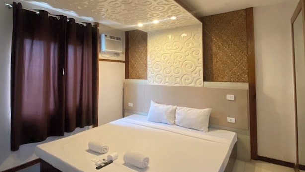 A modern hotel room with a large bed, a ceiling light fixture, and a wall-mounted air conditioning unit. - Villa Rosita Hotel Naga City (Naga)