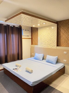 Ein modernes Hotelzimmer mit einem großen Bett, einem Bettkopfteil mit strukturierter Gestaltung, einer Wand-Klimaanlage und einem Vorhang.