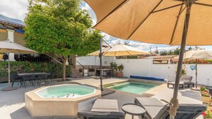 Un espace piscine extérieur comprenant un jacuzzi, des chaises longues et des parasols.