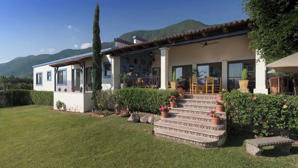 Une maison à deux étages avec un balcon, un escalier orné de plantes en pot et une vue sur les montagnes en arrière-plan.