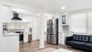 A modern kitchen with white cabinetry, a stainless steel refrigerator, and a black leather sofa in the living area. - House - Minutes from Siesta Key! (Sarasota)