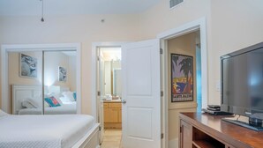 A hotel room with a bed, a TV, a bathroom, and a door leading to another room. - Coastal Two Bedroom Condo with Spectacular Views of the Bay, Gulf and Ono Island (Orange Beach)