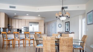 A modern kitchen with wooden cabinets, a dining area with wicker chairs, and a chandelier. - Coastal Two Bedroom Condo with Spectacular Views of the Bay, Gulf and Ono Island (Orange Beach)