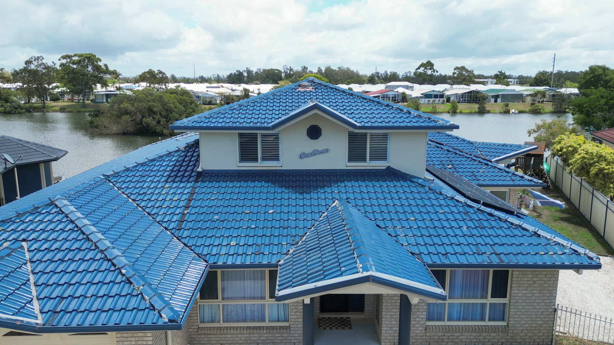 A house with a blue tiled roof, a central chimney, and a view of a lake.