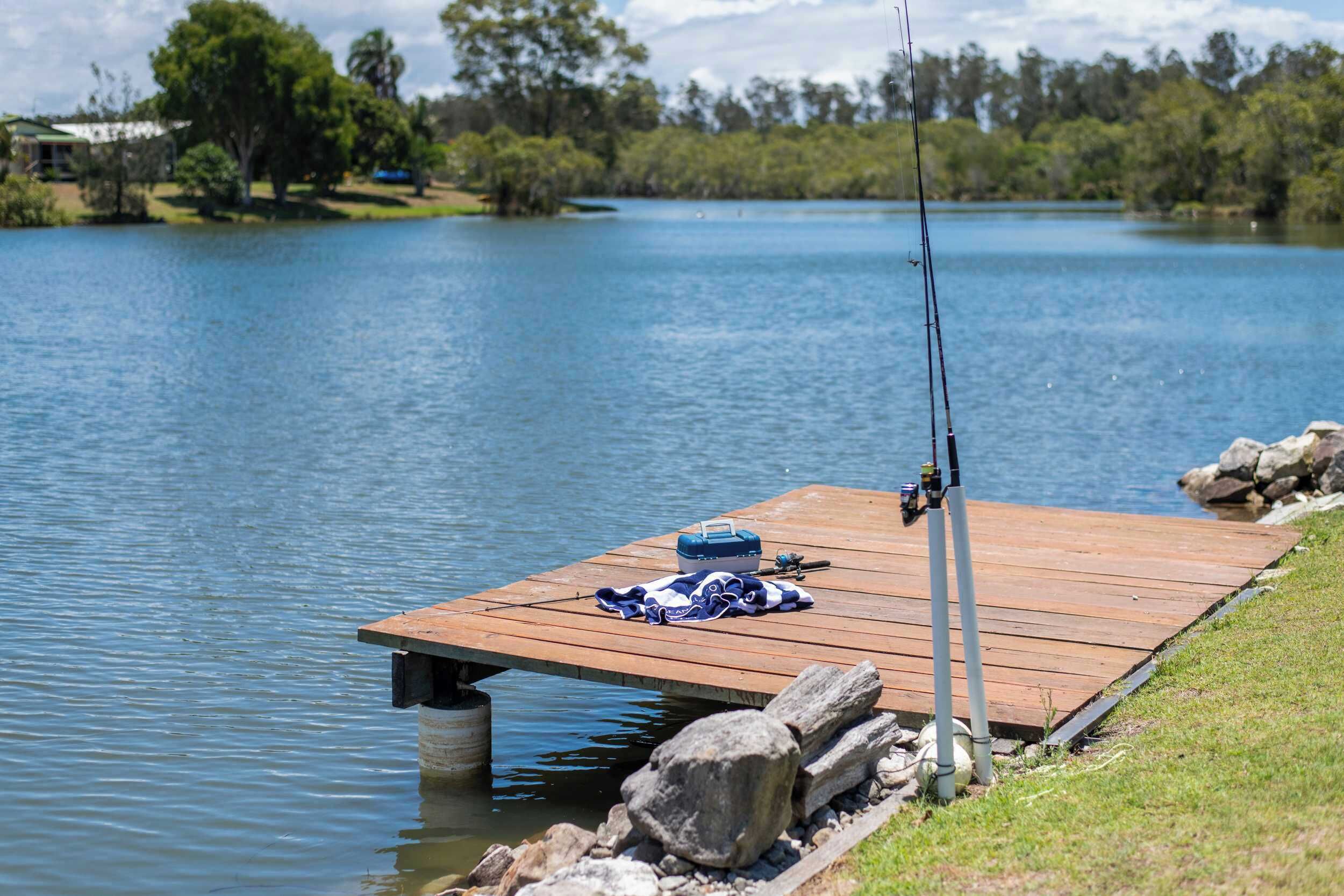 A wooden dock extending into a lake with fishing rods and a cooler on it.