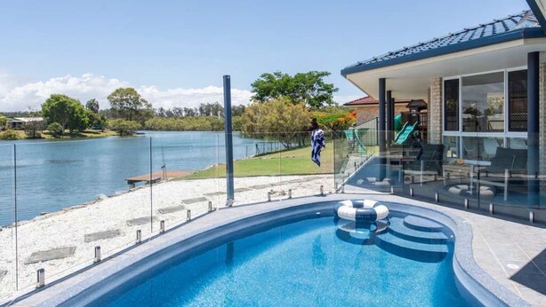 Une piscine avec vue sur un lac, un patio couvert et un bâtiment doté de grandes fenêtres.