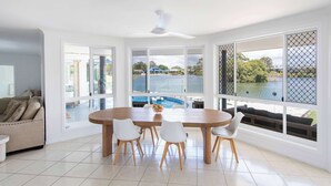 Une pièce spacieuse avec une grande table à manger, des chaises blanches et de grandes fenêtres donnant sur une piscine et un espace verdoyant.