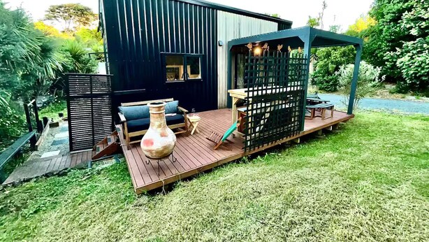 Un patio moderno al aire libre con terraza de madera, zona de estar con sofá y una mesa, y un jarrón decorativo.