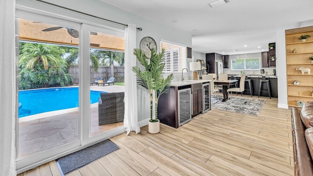 Ein modernes Wohnzimmer mit einem großen Schiebeglastür, die zu einem Poolbereich führt, einer Küche mit dunklen Schränken und einem Essbereich mit Teppich.
