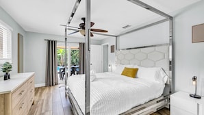 Ein modernes Schlafzimmer mit einem Himmelbett, einem Deckenventilator und Blick auf einen Außenpool-Bereich.