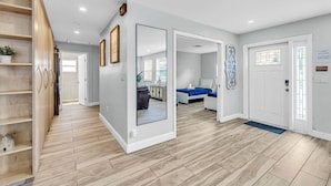 Ein modernes Interieur mit Holzboden, einem Flur, der zum Schlafzimmer mit Bett und blauer Akzentwand führt, und einer weißen Tür mit einem Schild.