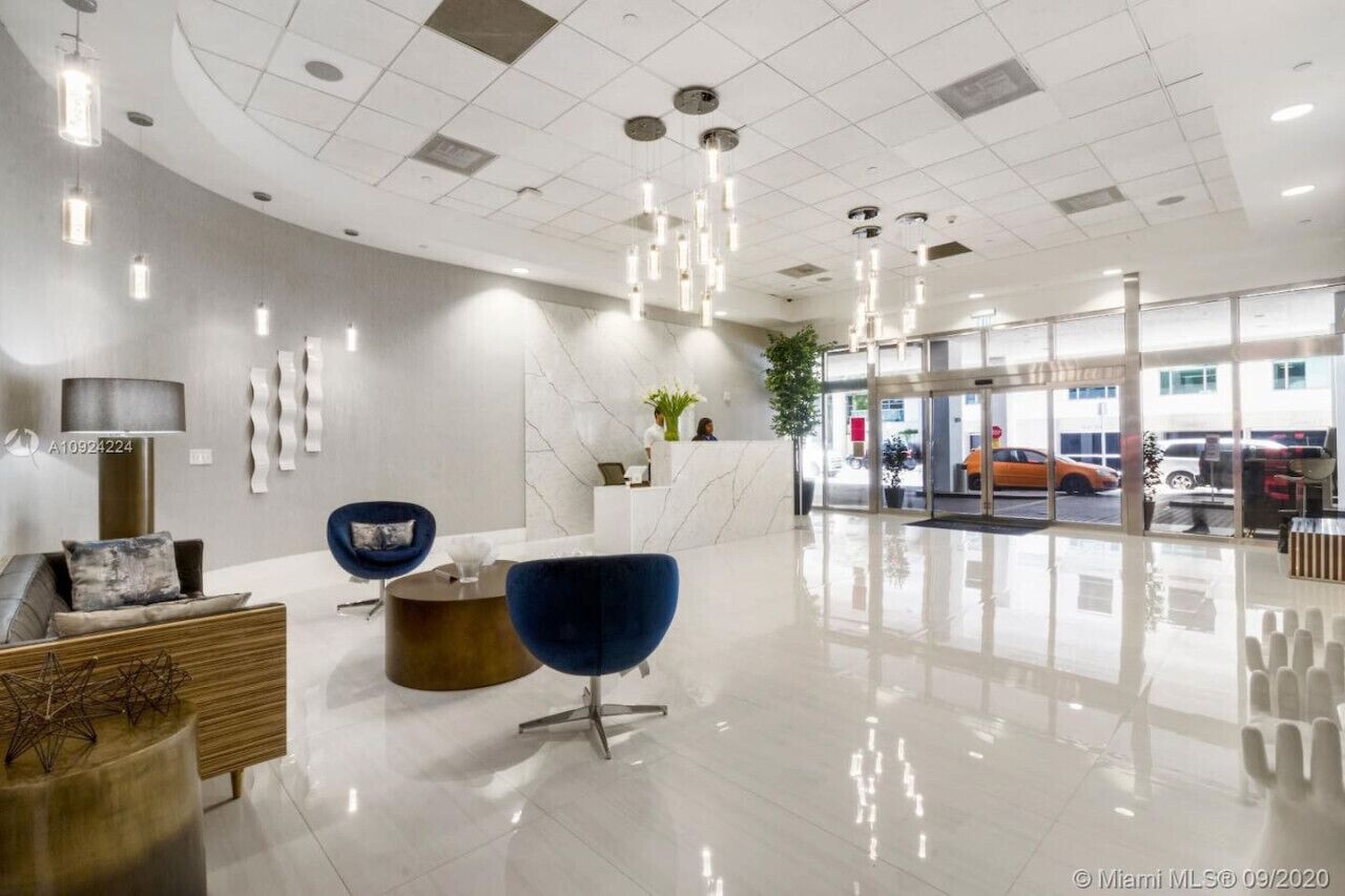 Un hall d’entrée moderne avec un comptoir d’accueil, un espace salon et une entrée en verre.