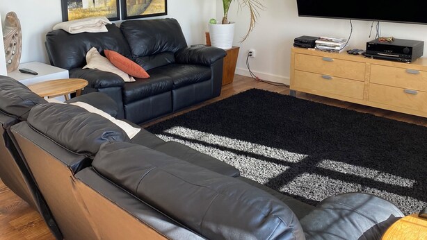A modern living room with a black leather sofa, a large flat-screen TV, and a wooden cabinet.