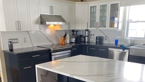 A modern kitchen with white cabinets, a large island with bar stools, stainless steel appliances, and a window providing natural light.