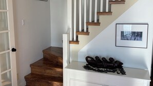 A staircase with wooden steps and white railings, a white bench with decorative items, and a door with frosted glass panels.