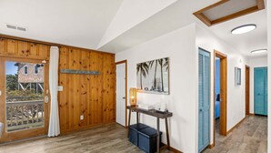 Ein Flur mit Holzboden, einer Holztür, einem an der Wand hängenden Bild, einem kleinen Tisch mit einer Lampe und einer blauen Tür.