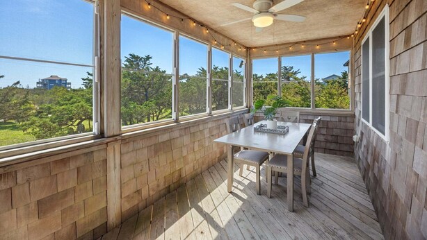 Eine überdachte Terrasse mit Tisch und Stühlen, großen Fenstern und einem Deckenventilator.