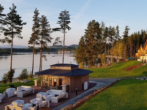 A lakeside lodge with outdoor seating, a small building with large windows, and a view of the lake and surrounding trees. - Lakeside Village 18 by Interhome (Frymburk)