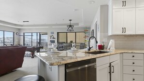 Une cuisine moderne avec des meubles blancs, un lave-vaisselle et un coin repas comprenant un canapé rouge et une vue sur la ville.