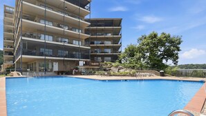 Un immeuble à plusieurs étages doté de balcons, d’une piscine et d’un arbre.