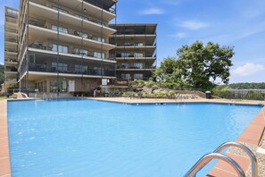 Un edificio a più piani con balconi, una piscina e un albero.
