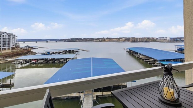 A waterfront view with a dock area, a covered boat launch, and a building in the background. - Land's End #732 Gorgeous Remodel! Parking Level! (Osage Beach)