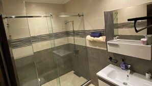 A modern bathroom with a glass-enclosed shower, a white sink, and a mirror above it. - Cosy seaside apartment (Tanger)