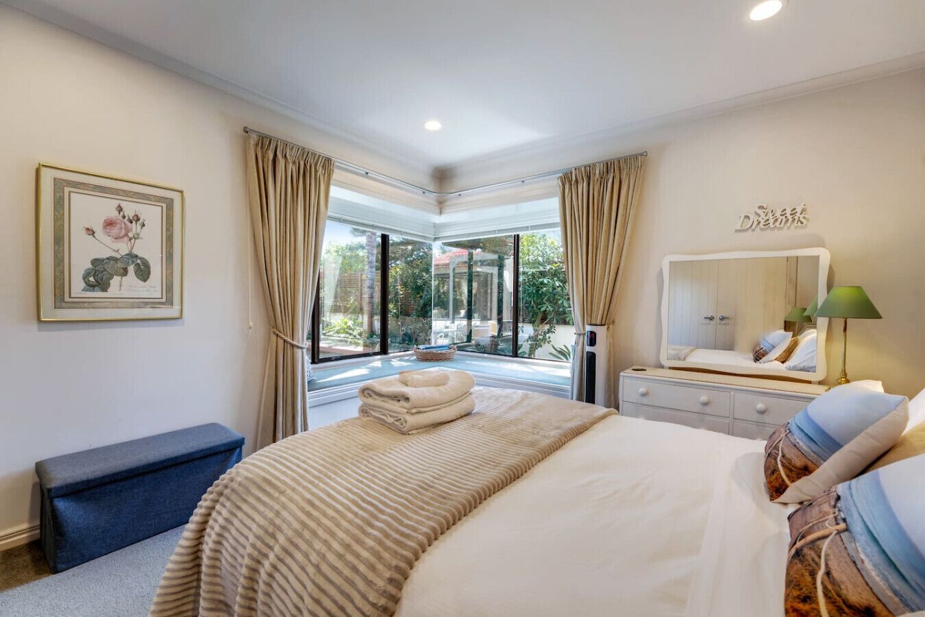 Une chambre à coucher avec un grand lit, une table de chevet, un miroir et une fenêtre avec des rideaux.