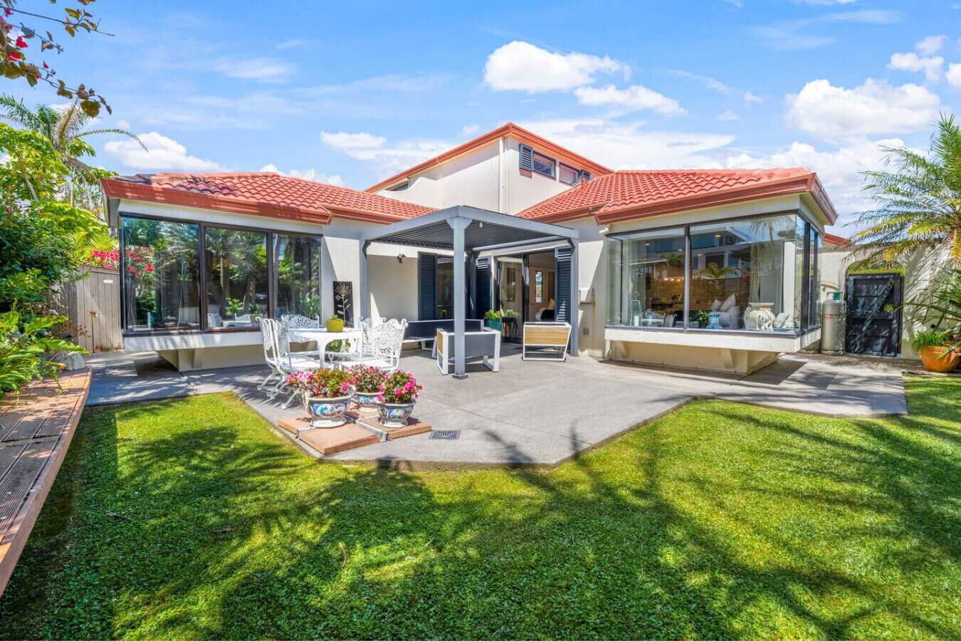 Une maison moderne dotée d’un patio couvert, d’une pelouse et de plantes en pot.