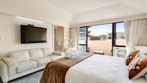 A hotel room with a bed, a sofa, a TV, and a balcony with a view. - Orewa Beachside Escape | Backyard & BBQ (Auckland Hibiscus Coast)
