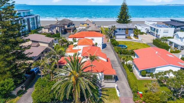 An aerial view of a coastal residential area with houses, a beach, and a clear sky. - Orewa Beachside Escape | Backyard & BBQ (Auckland Hibiscus Coast)