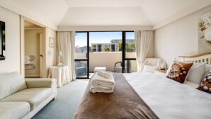 A hotel room with a bed, a sofa, a small table, and a view of the outdoors through large windows. - Orewa Beachside Escape | Backyard & BBQ (Auckland Hibiscus Coast)