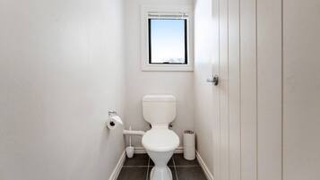 A small, clean bathroom with a toilet, a toilet paper holder, a window, and a trash can.