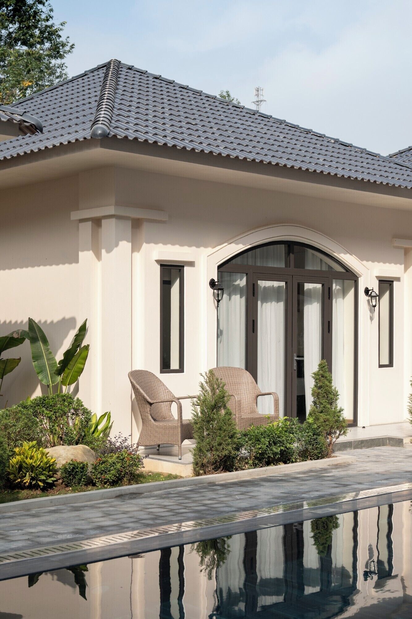A house with a swimming pool, a covered patio with chairs, and a garden with various plants.
