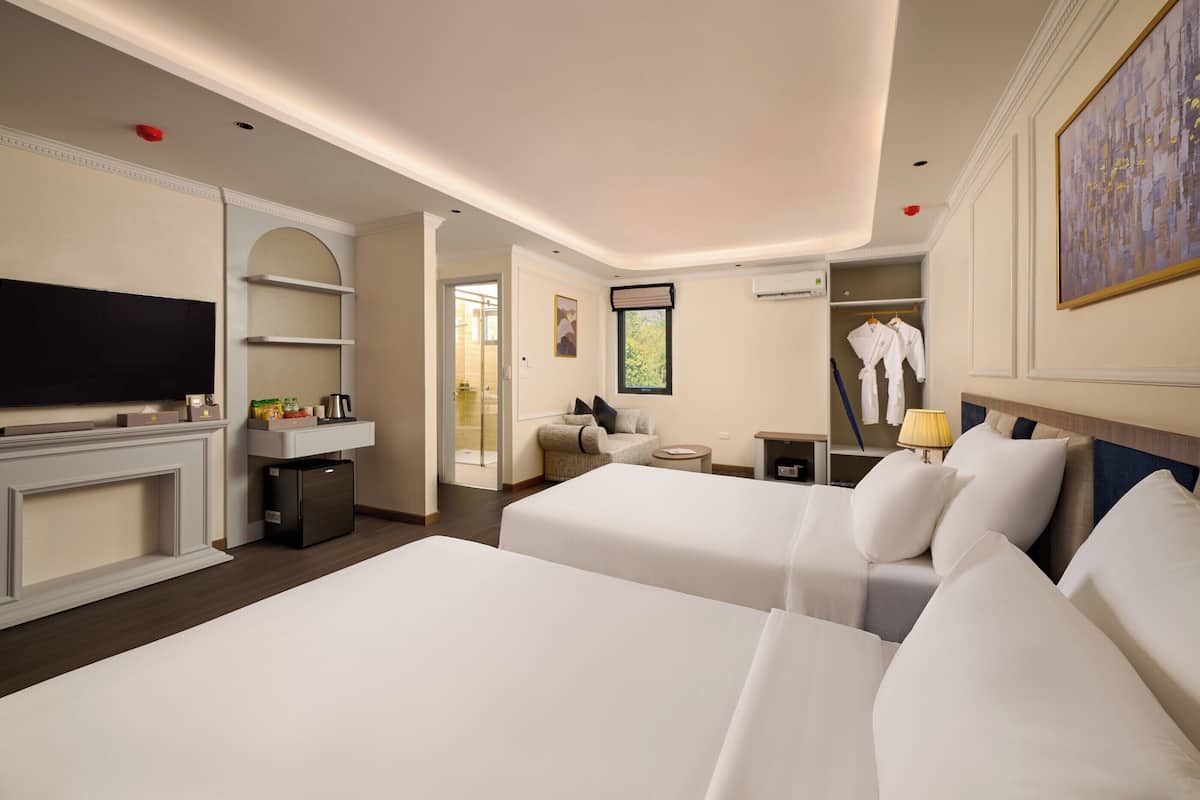 A hotel room with two beds, a TV, a desk, a chair, a robe, and a coat rack.