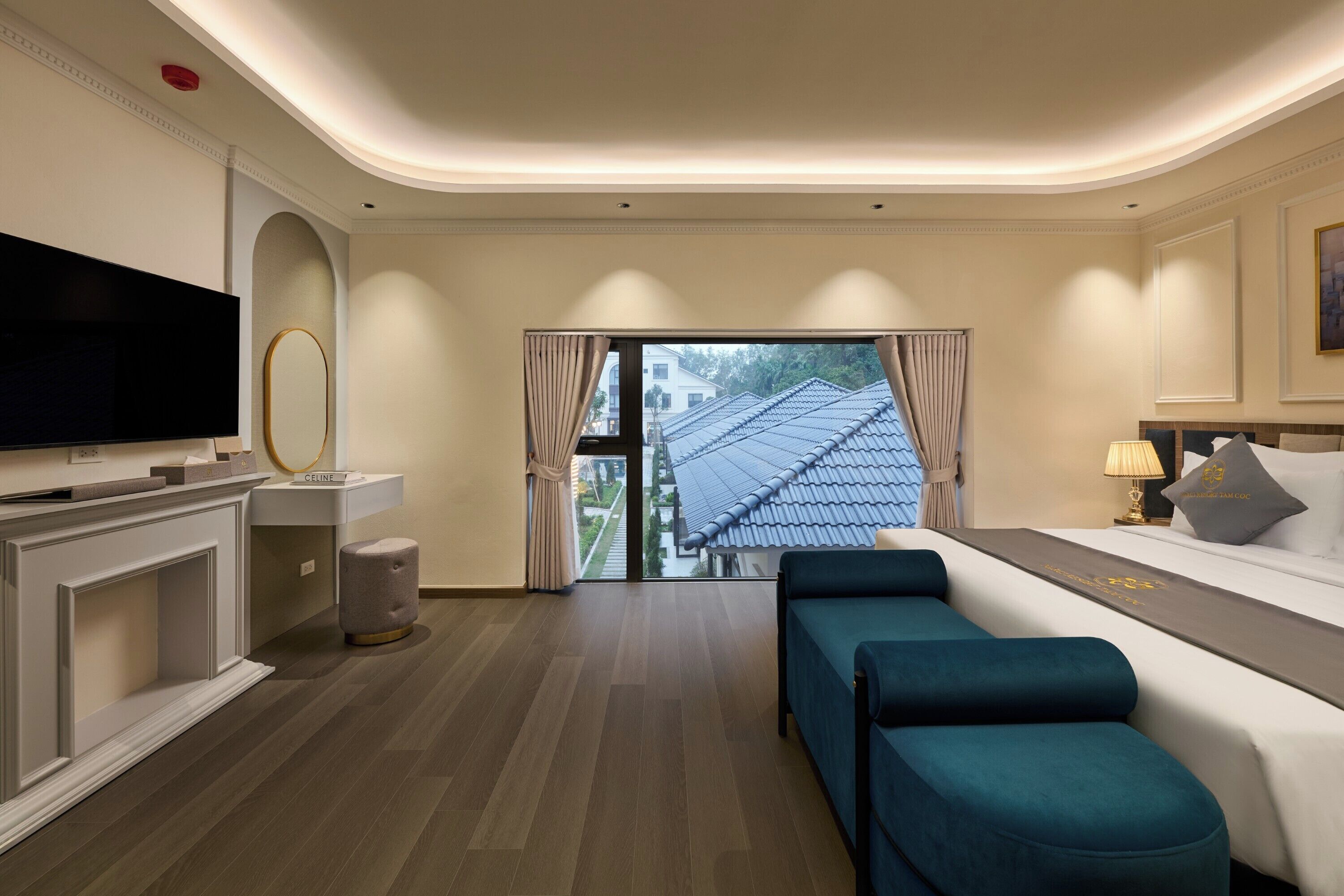 Quarto de hotel moderno com televisão de tela plana, sofá, cama com cabeceira e vista para um edifício tradicional por uma grande janela.