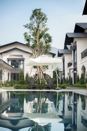 Una piscina amb el reflex d'edificis i un arbre.