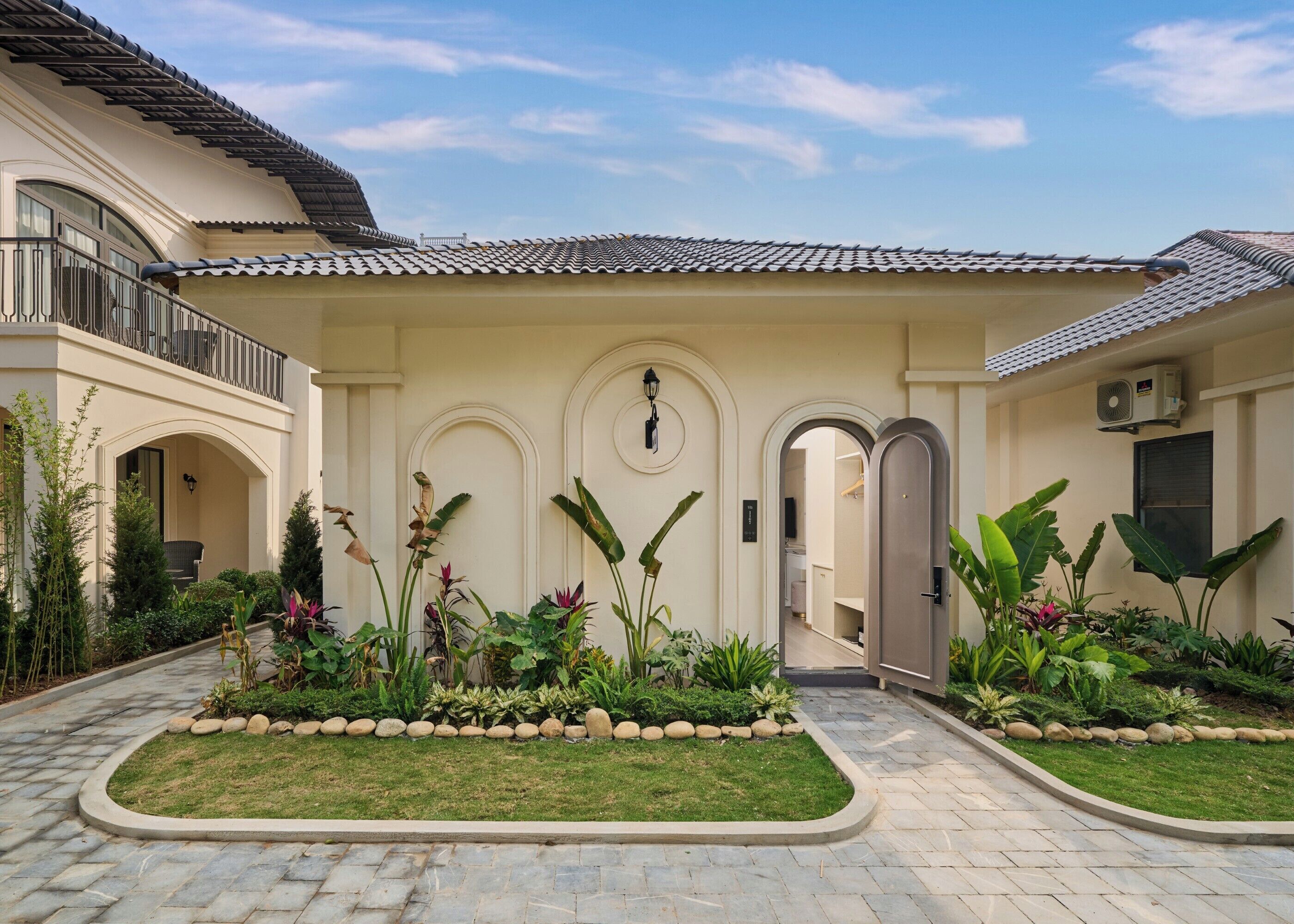 A building with a tiled roof, a covered entrance, and a garden with various plants and a paved walkway.