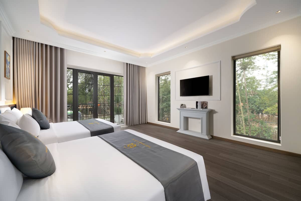 A modern hotel room with two beds, a TV, and large windows offering a view of the outdoors.