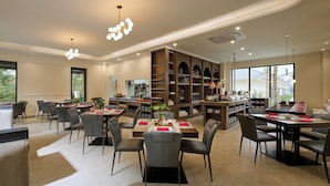 A spacious dining area with multiple tables and chairs, a large bookshelf, and a kitchen area in the background.