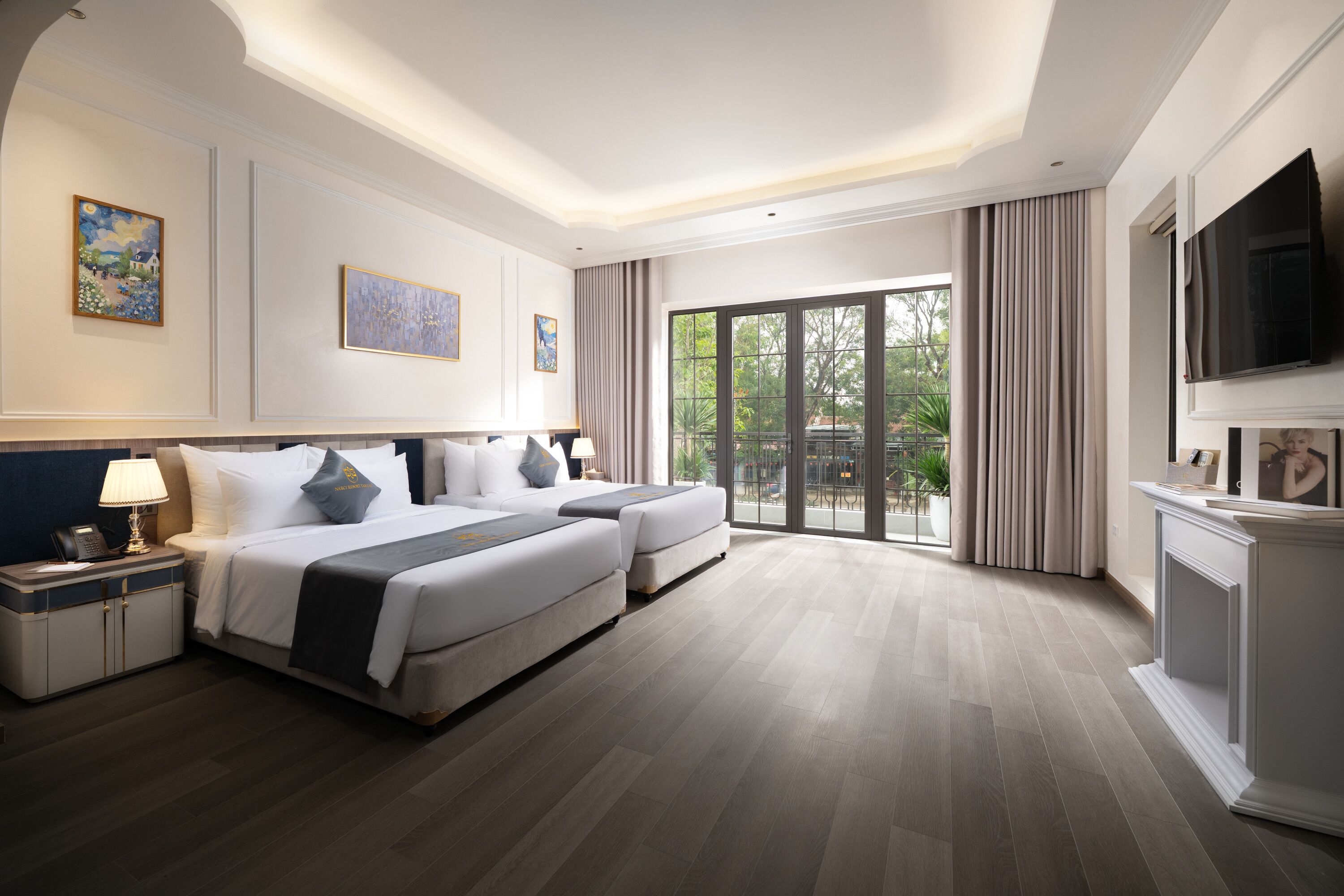 A hotel room with a large bed, two bedside tables, a TV, and a balcony with curtains.
