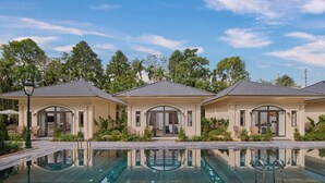 A resort with three villas, each with a tiled roof and large windows, connected by a pool with clear water.
